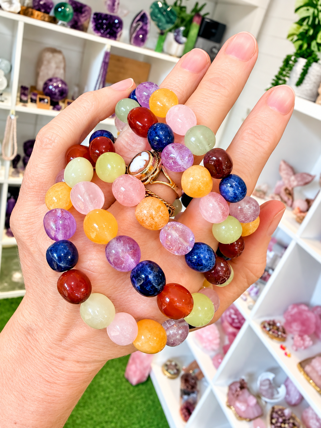 Colourful mixed gemstone chakra bracelets held in hand with crystal shop background 